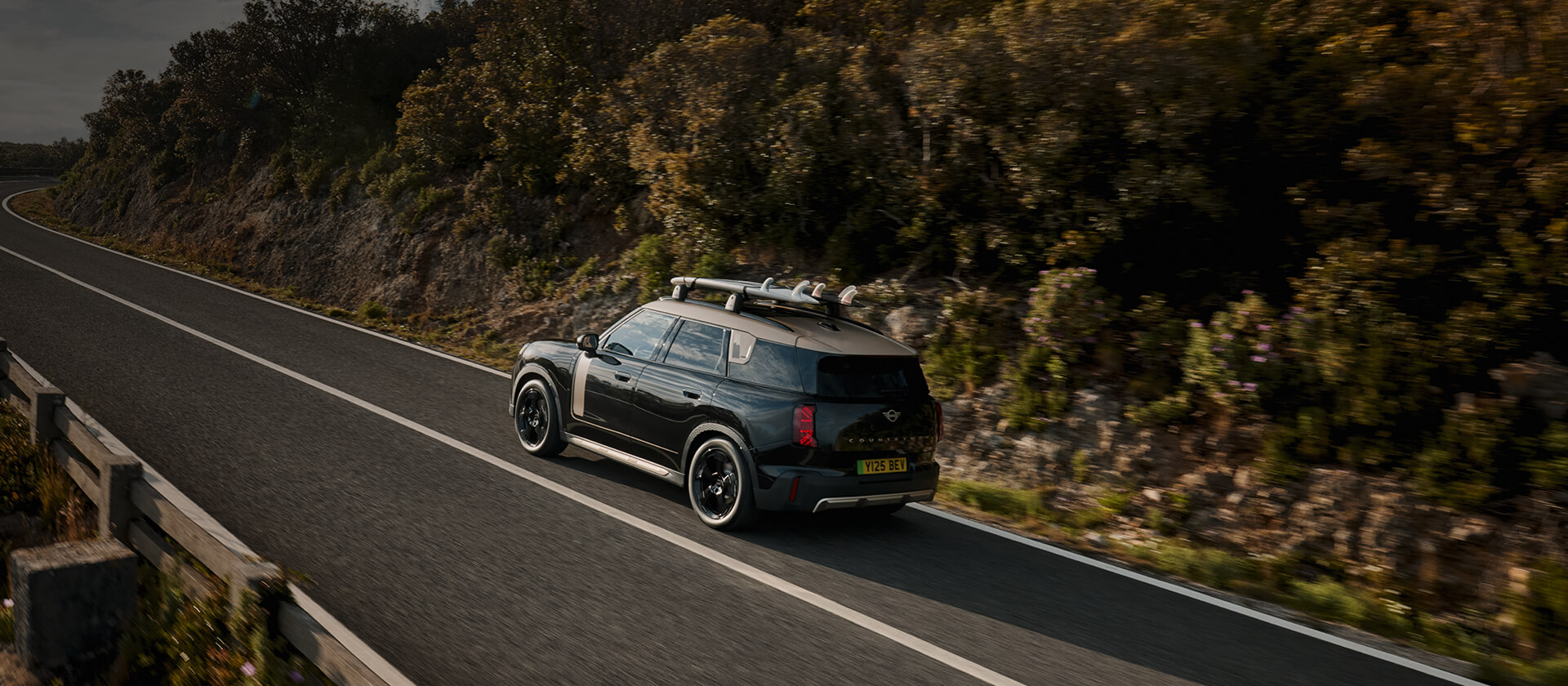 MINI Countryman in Heck-Seitenansicht während der Fahrt auf einer Landstraße.