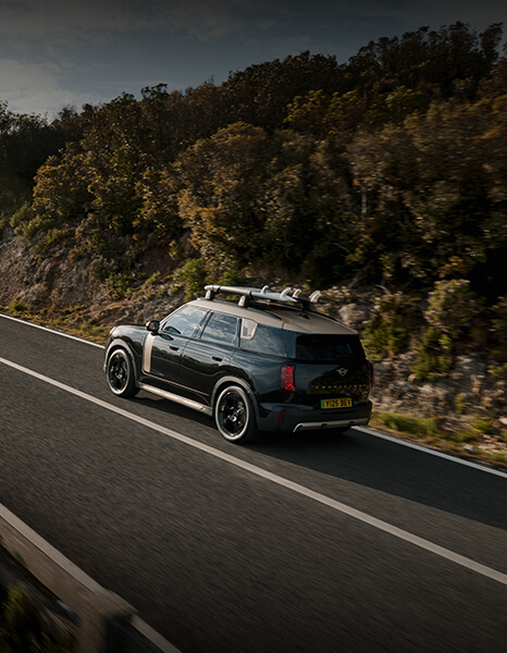 MINI Countryman in Heck-Seitenansicht während der Fahrt auf einer Landstraße.