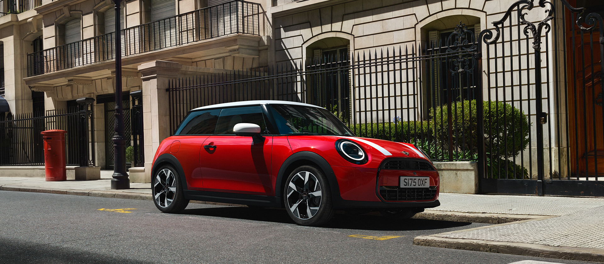 Roter MINI Cooper mit weißem Dach in Seitenansicht an einer städtischen Straße.
