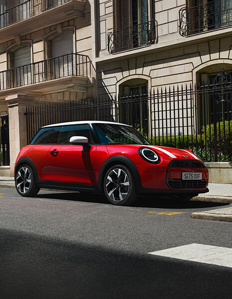 Roter MINI Cooper mit weißem Dach in Seitenansicht an einer städtischen Straße.
